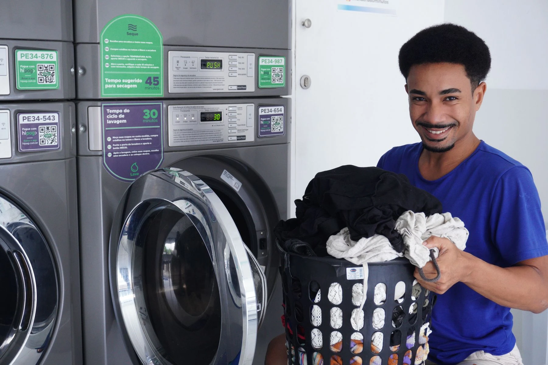 Laki-laki tersenyum membawa keranjang pakaian di laundromat - foto stok ilustratif, bukan staf atau lokasi Bening Laundry